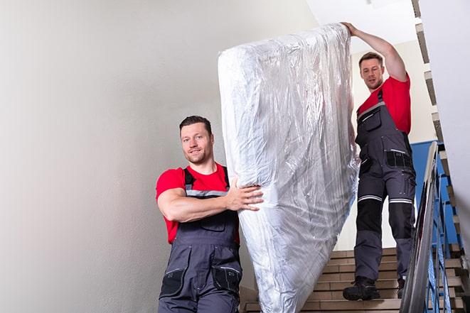 two people carrying a box spring out of a bedroom in Dansville, MI